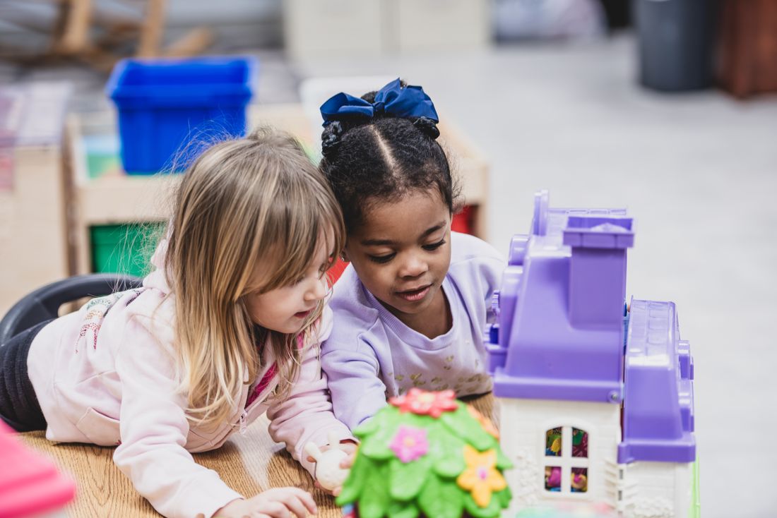 Two girls lean in close to play with a purple dollhouse