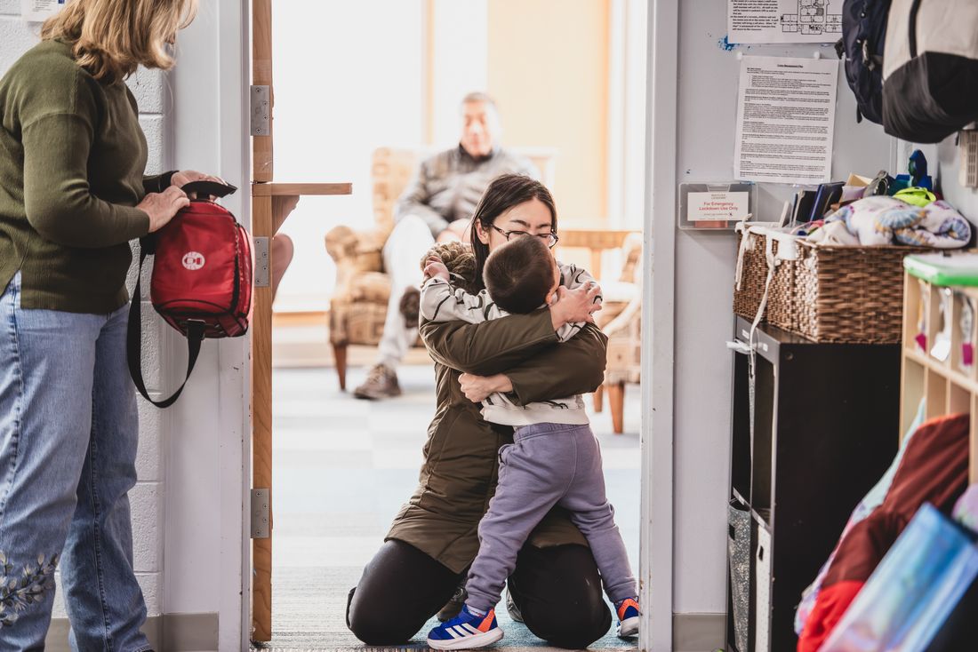 A parent kneels in the doorway and hugs a small boy at pick-up time