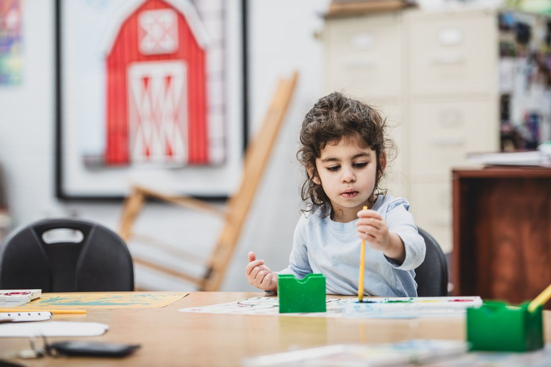 A preschooler paints at a table with green paint cups