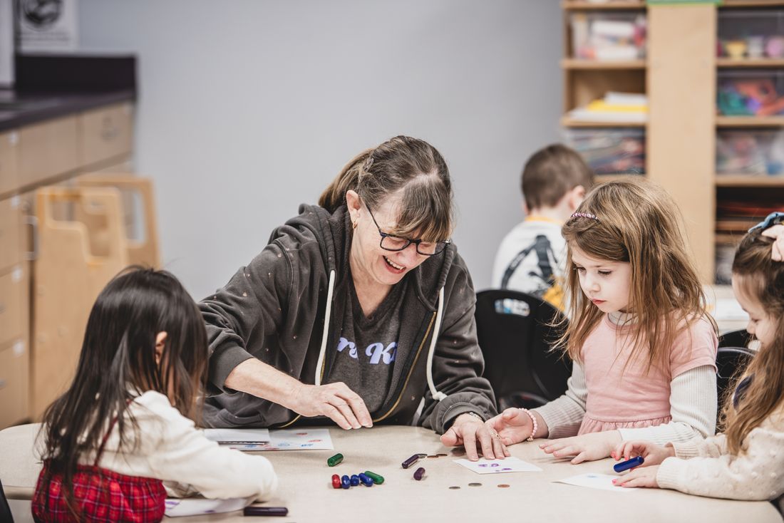 A teacher laughs with three girls sorting colored pieces at a table