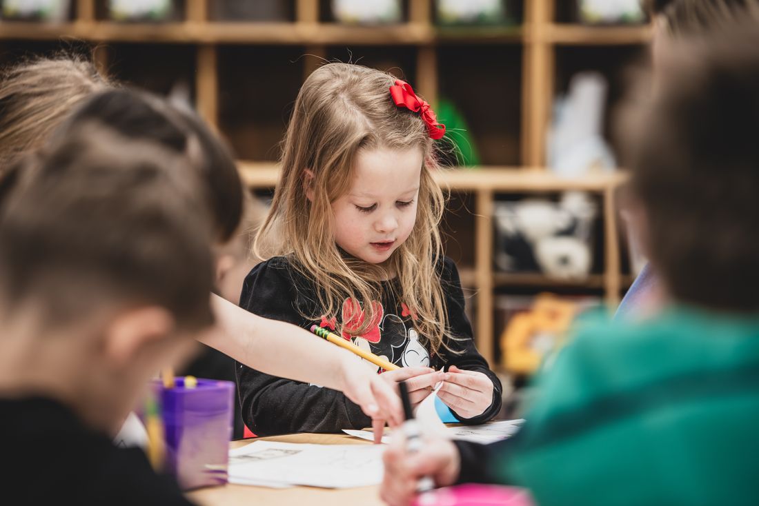 A girl with a red bow writes carefully at a table