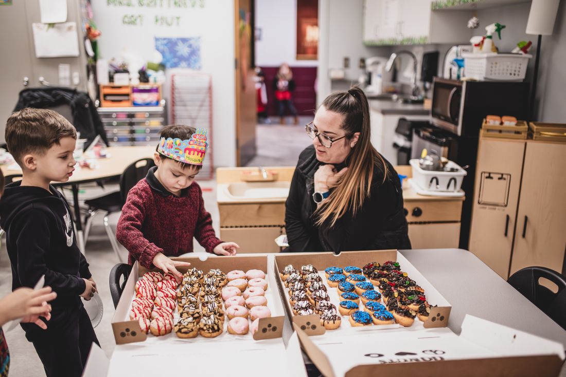 A teacher and two boys look over boxes of decorated donuts for a party