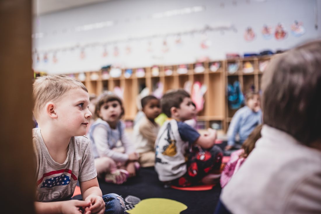 A boy on the rug smiles at a classmate during circle time