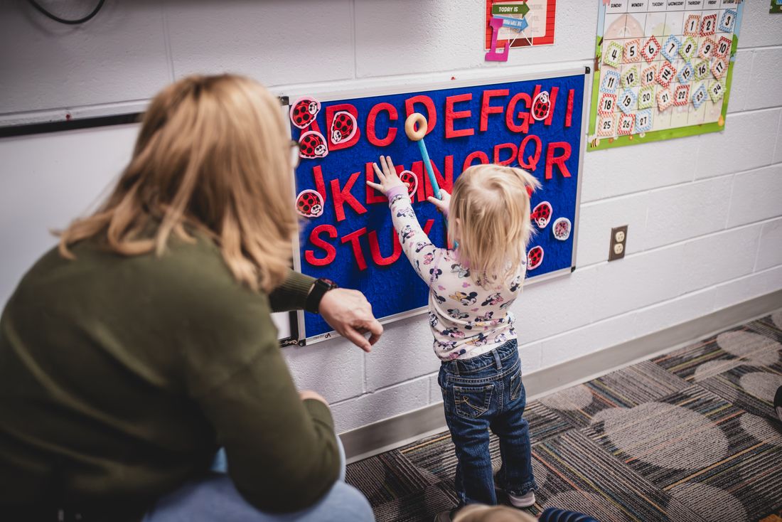 A toddler places felt letters on a blue alphabet board