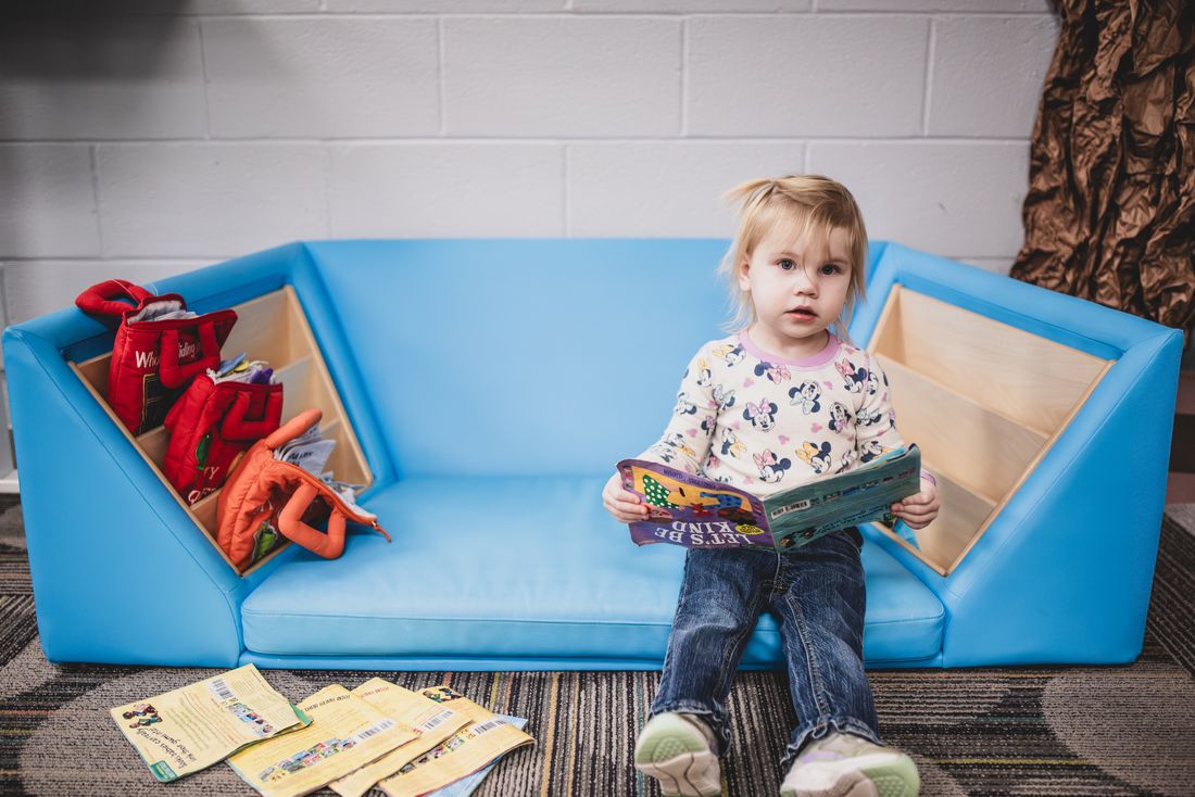 A toddler sits on a bright blue soft couch holding a picture book