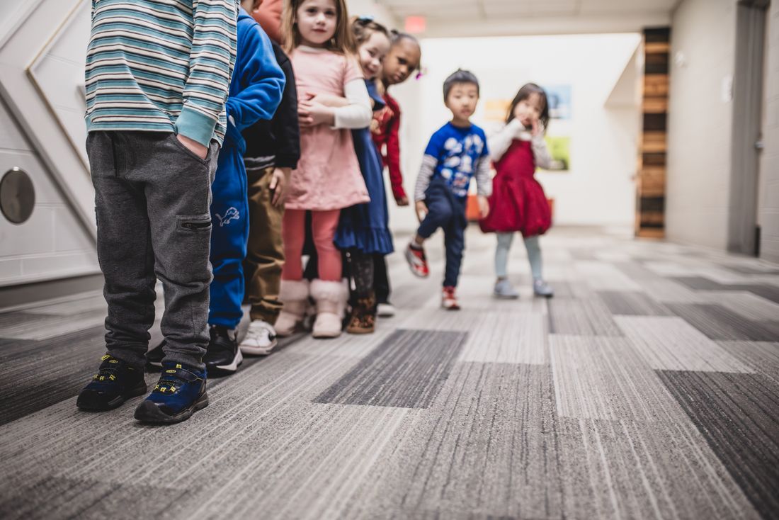 A line of preschoolers walks down the hallway toward the camera